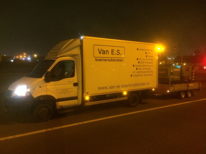Een Van E.S. koeriersbus met aanhanger levert 's nachts een generator af bij een klant.